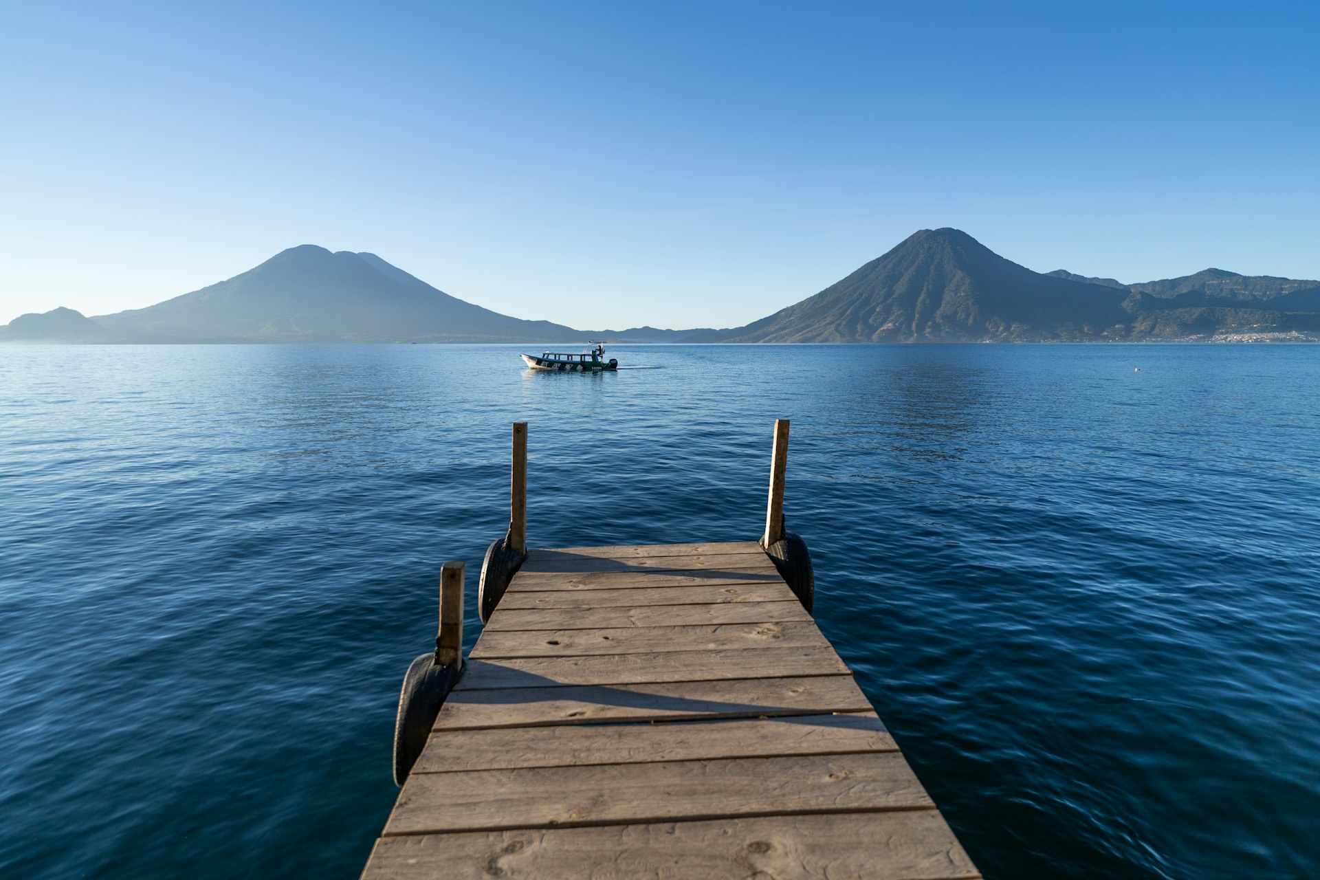 a dock leading out to a boat in the water with Lake Atitlán in the background